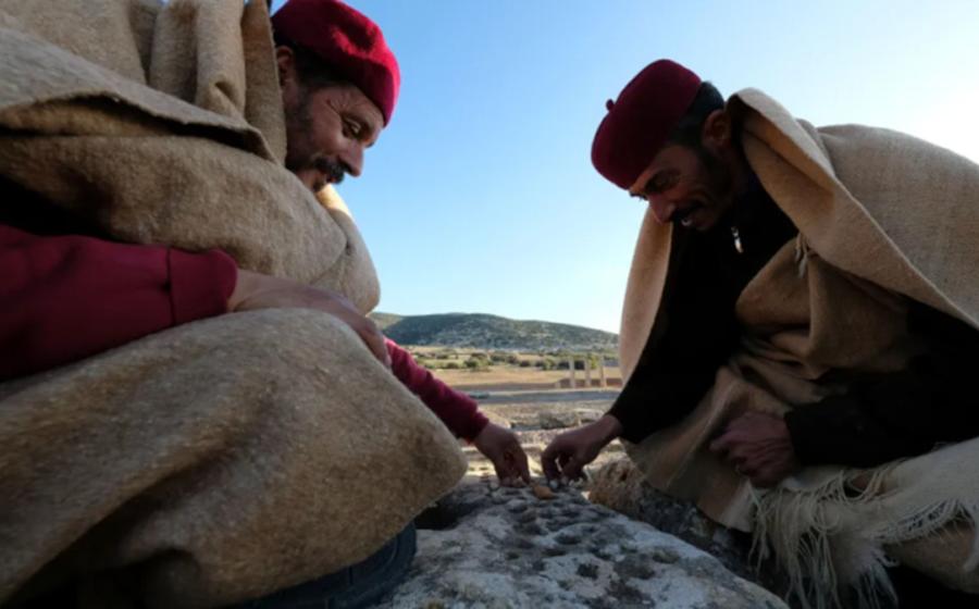 Residents of Tolmeita, dressed in traditional costumes, play a game on the walls within the Cistern Square in Ptolemais